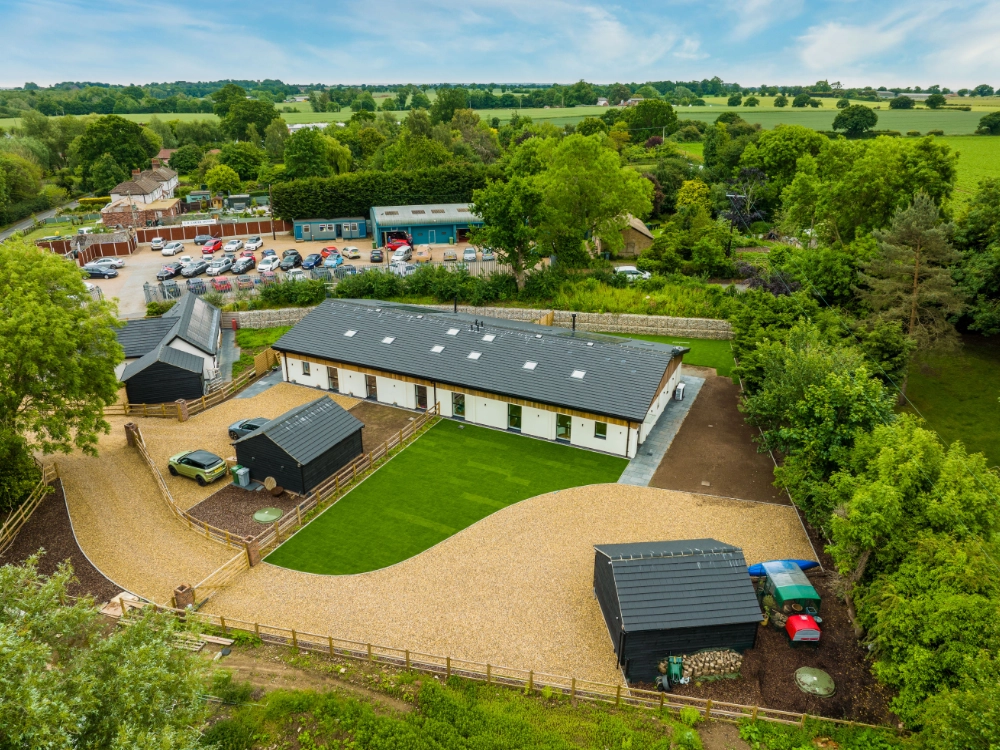 Aerial view of a countryside property with gravel driveway, outbuildings, green lawns, and surrounding fields