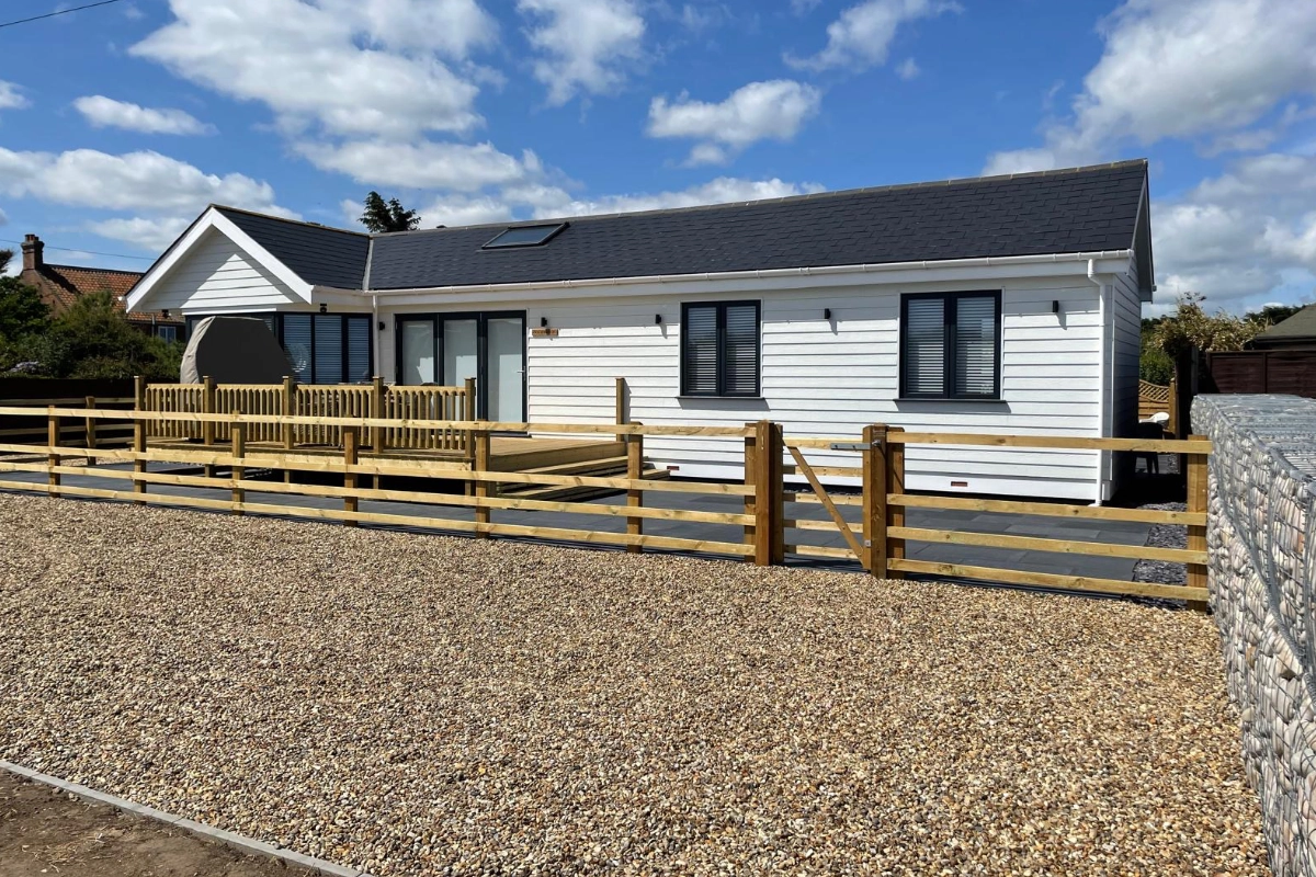 White countryside holiday lodge with gravel driveway, wooden fencing and blue sky
