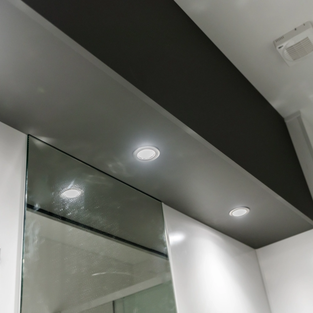 Modern bathroom ceiling with recessed spotlights, dark ceiling panel and glass shower screen.