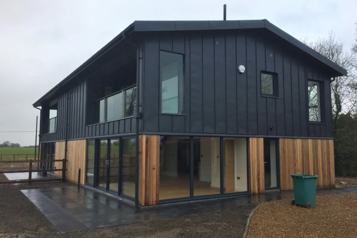 Modern two-storey house with black cladding, timber panels, large glass doors, and countryside surroundings