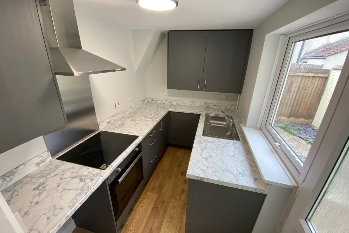 Modern fitted kitchen with grey cabinets, marble effect worktops, hob, sink and window