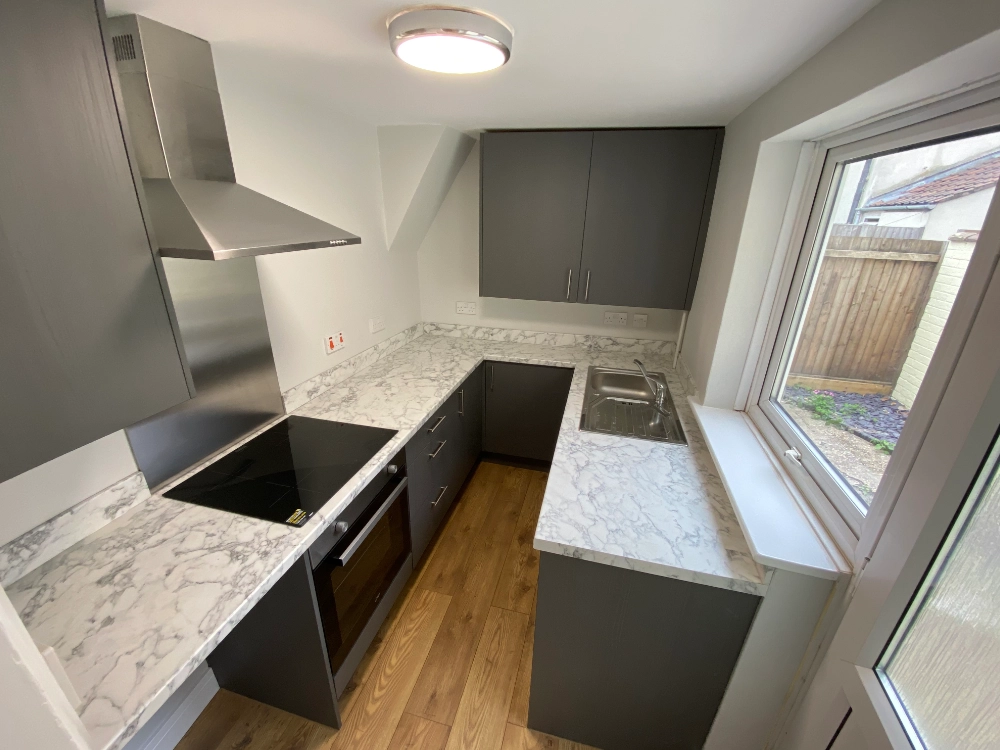 Compact modern kitchen with dark grey cabinets, marble effect worktops, sink, hob, and stainless steel extractor