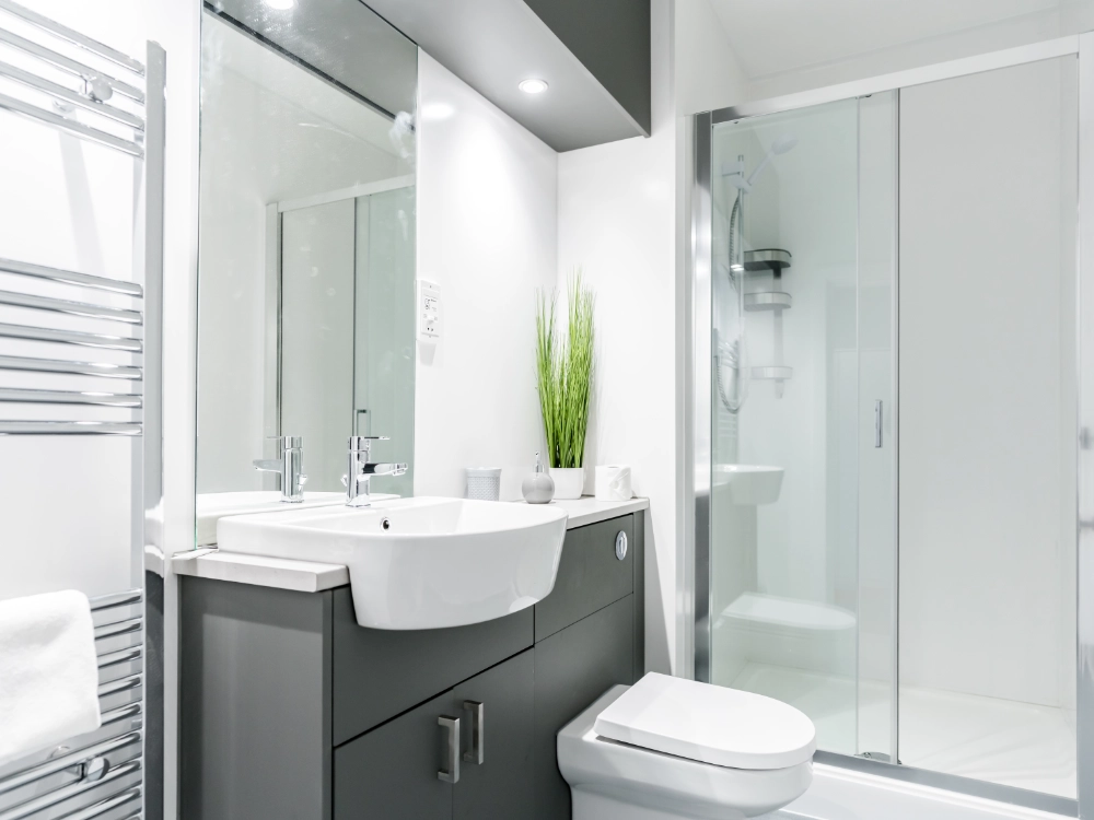 Modern white and grey bathroom with walk in shower, vanity unit, toilet, mirror, and chrome towel radiator