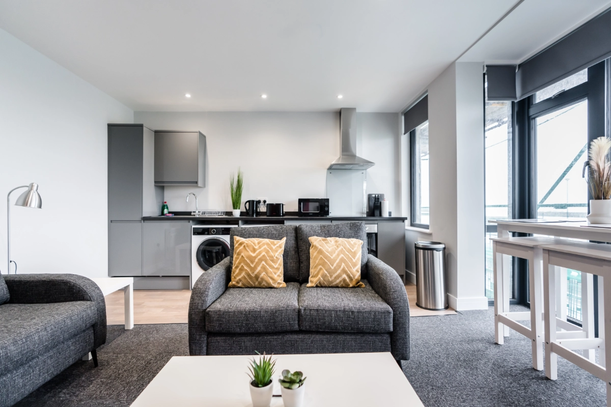 Modern open plan apartment living room with grey sofas, kitchen and balcony windows